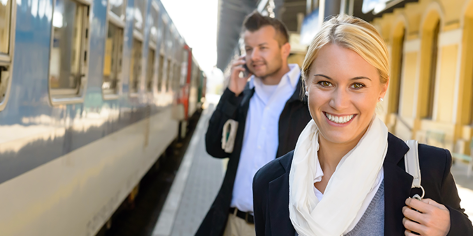 Smiling female, man on phone, business casual dress, waiting to board train at station