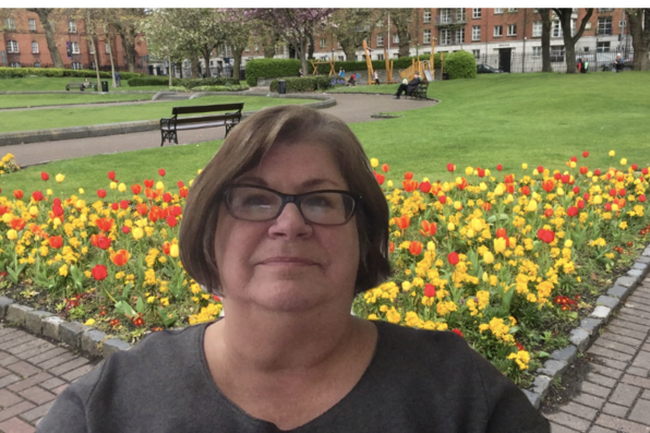 Mary Ayers with a virtual background of an orange and yellow flower bed